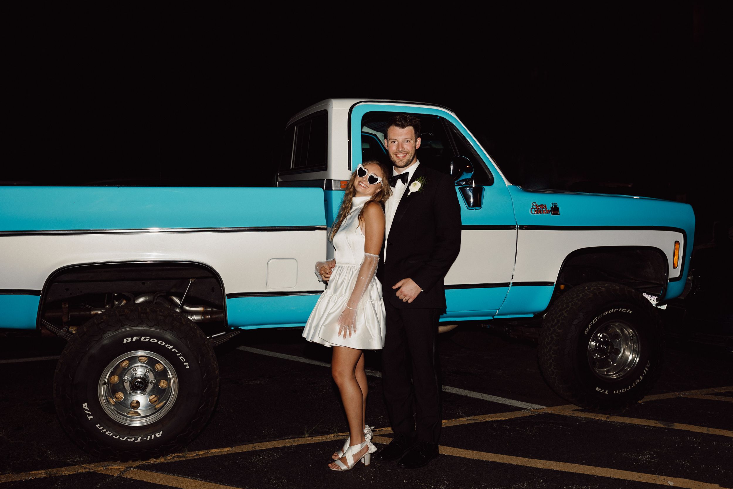Wedding couple poses next to a vintage turquoise car at night.
