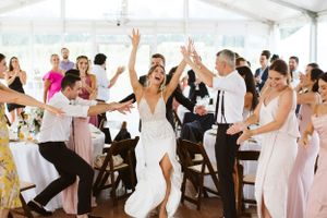 Wedding party celebrating with energetic dance moves under a white tent.