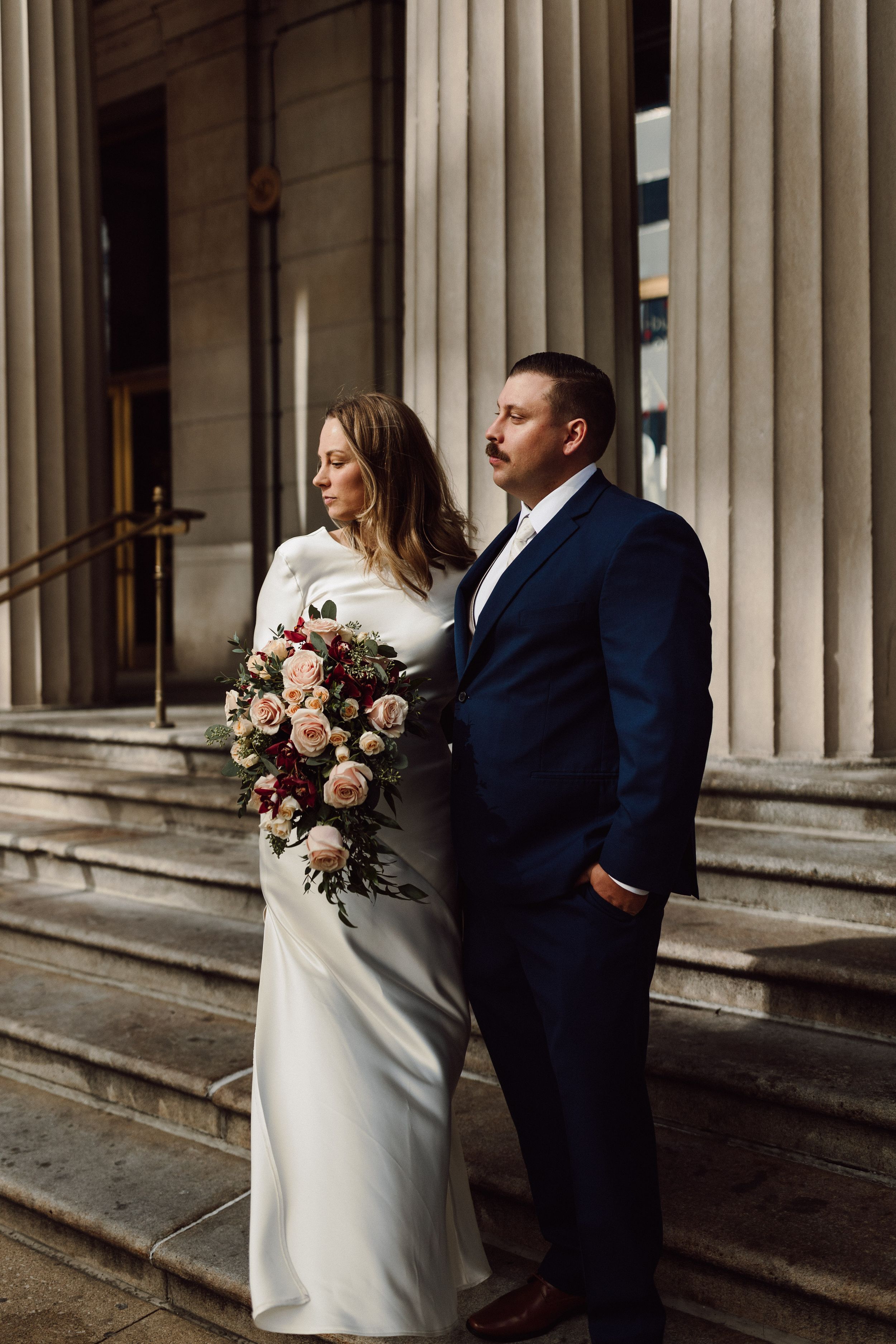 Elegant wedding couple poses against classic stone columns in front of Chicago Cultural Center