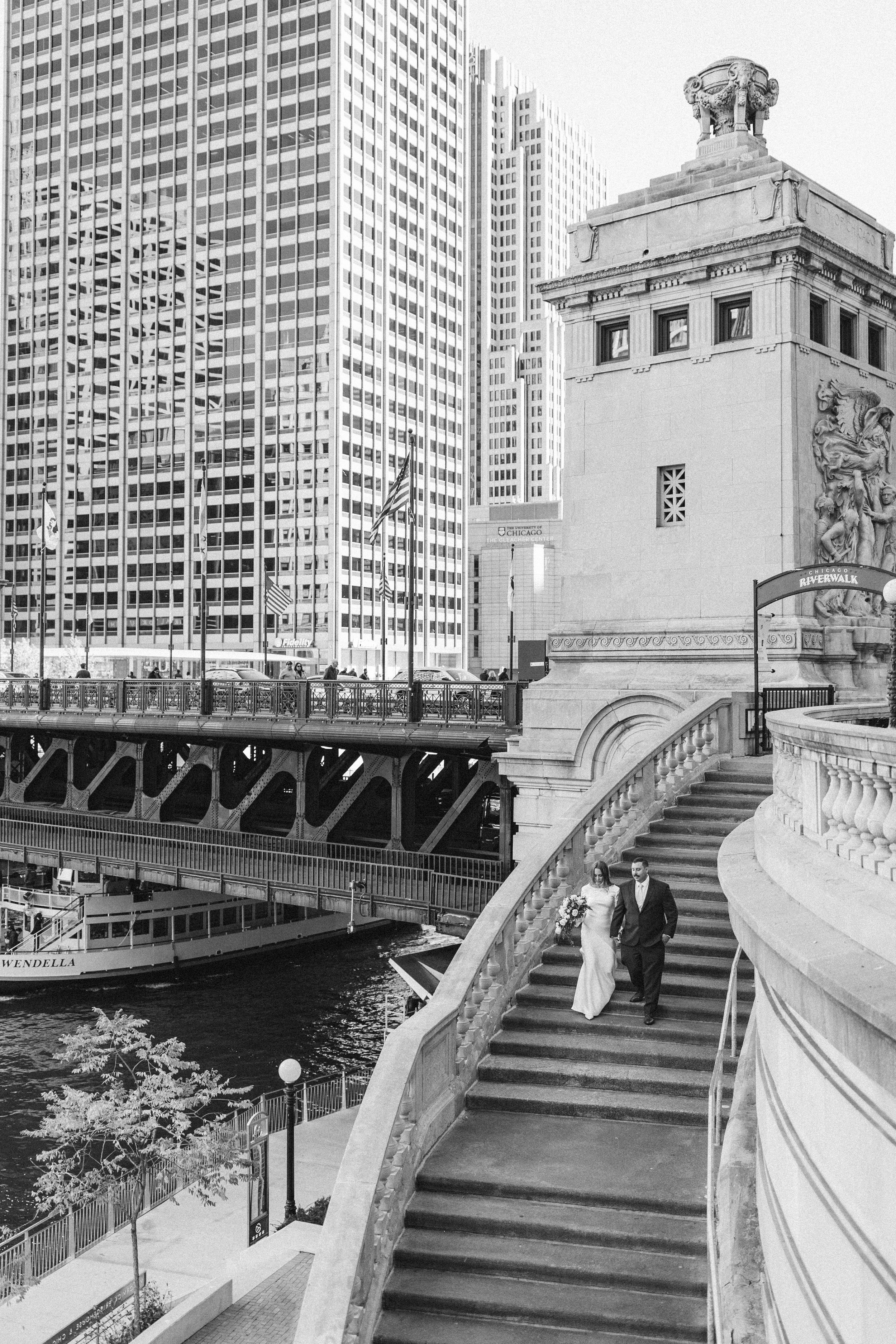 Black and white architectural wedding photo on Chicago Riverwalk bridge with city skyline.