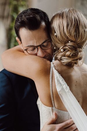 A tender wedding moment showing close-up details of a bride's beaded dress strap and intimate embrace.