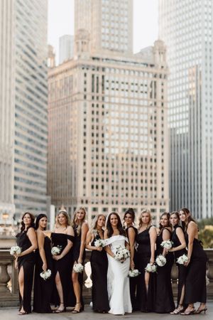 Bridesmaids in black dresses pose with bride against Chicago skyline.