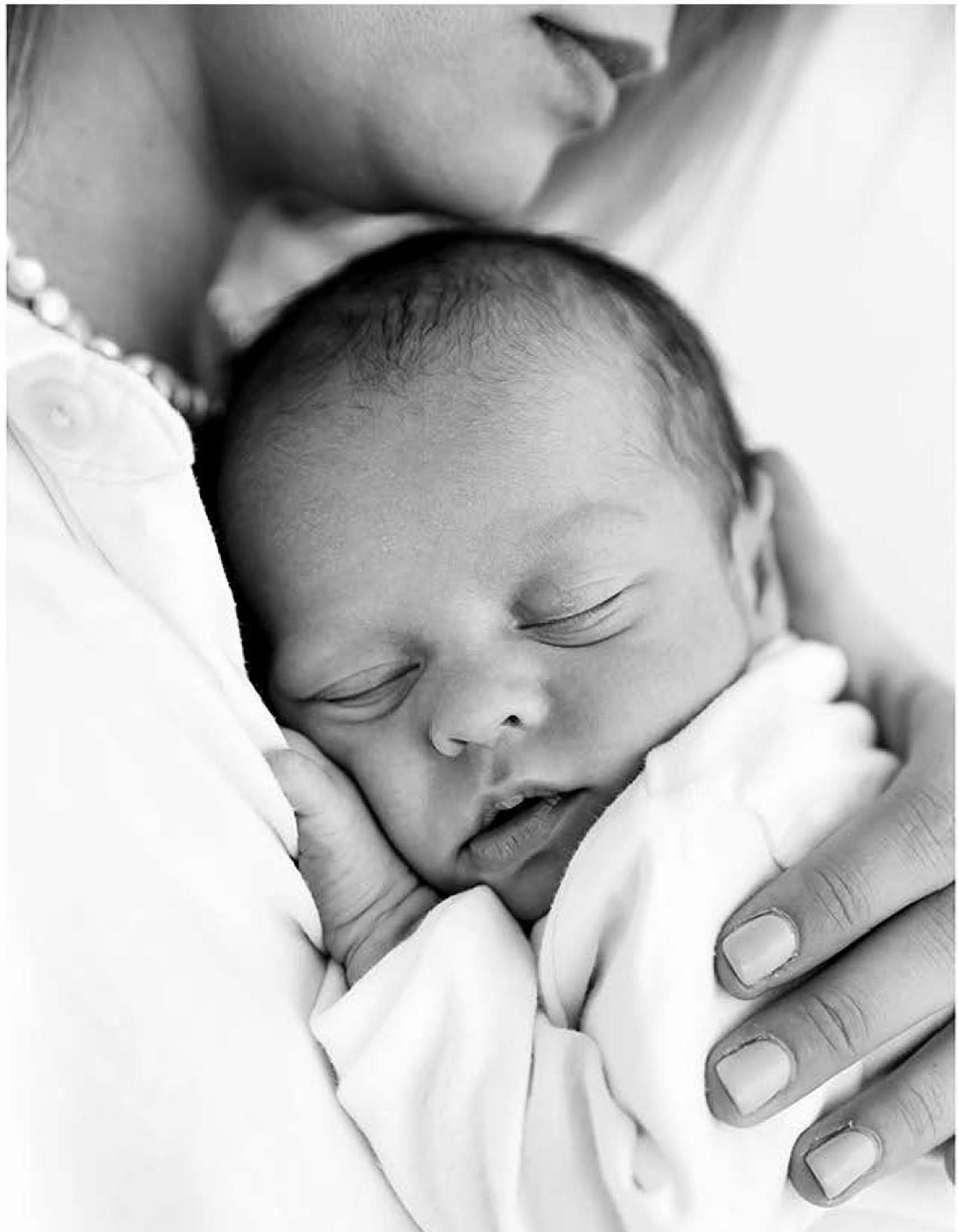 A peaceful black and white portrait of a sleeping newborn baby being gently cradled in white fabric.