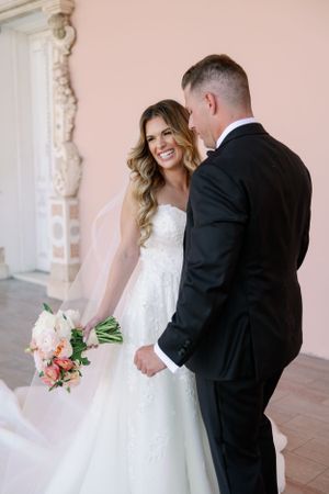 Happy bride in white lace gown shares a joyful moment with groom in black tuxedo while holding peach bouquet at the Ringling.