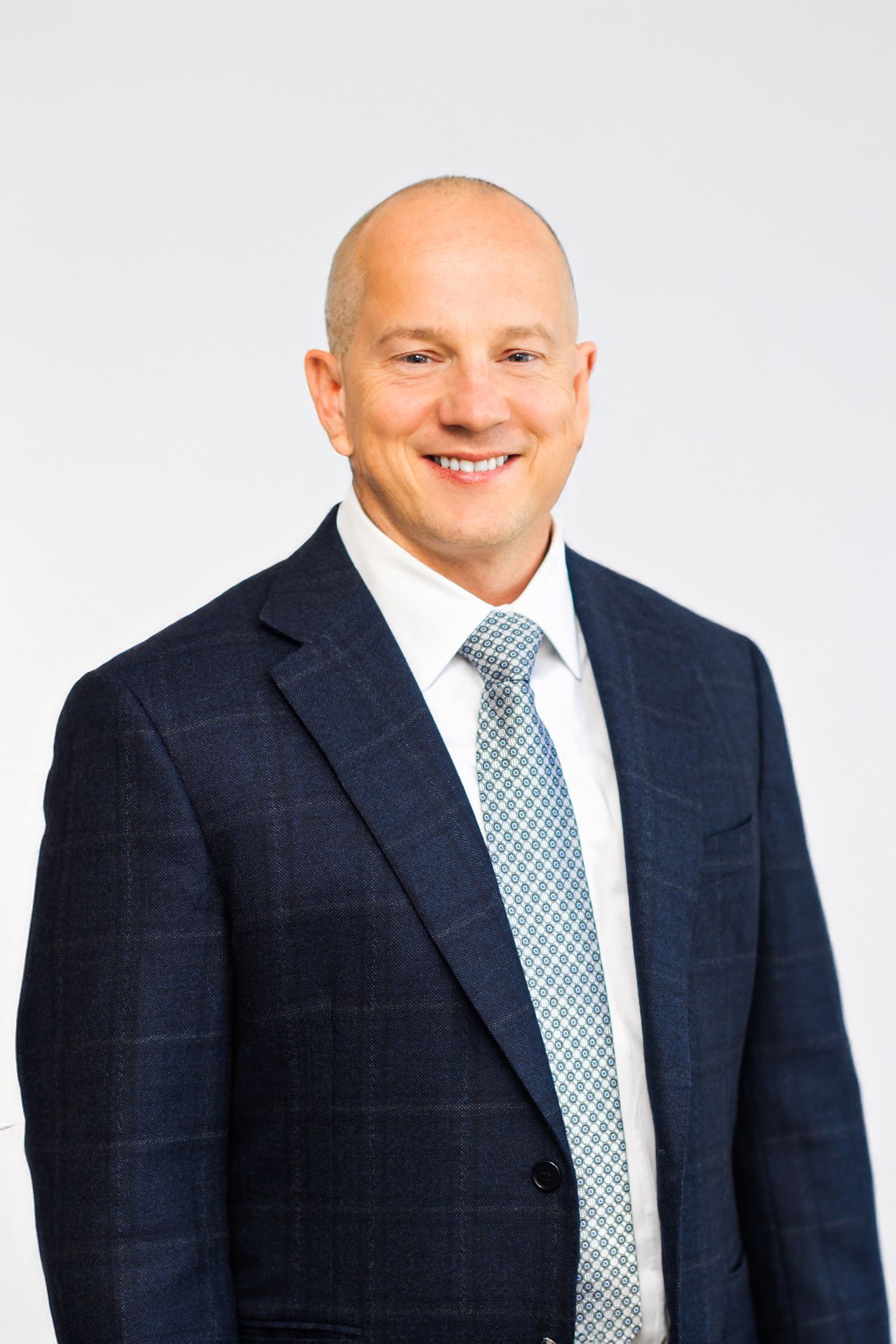 Professional headshots of man in black suit and white shirt against dark background.