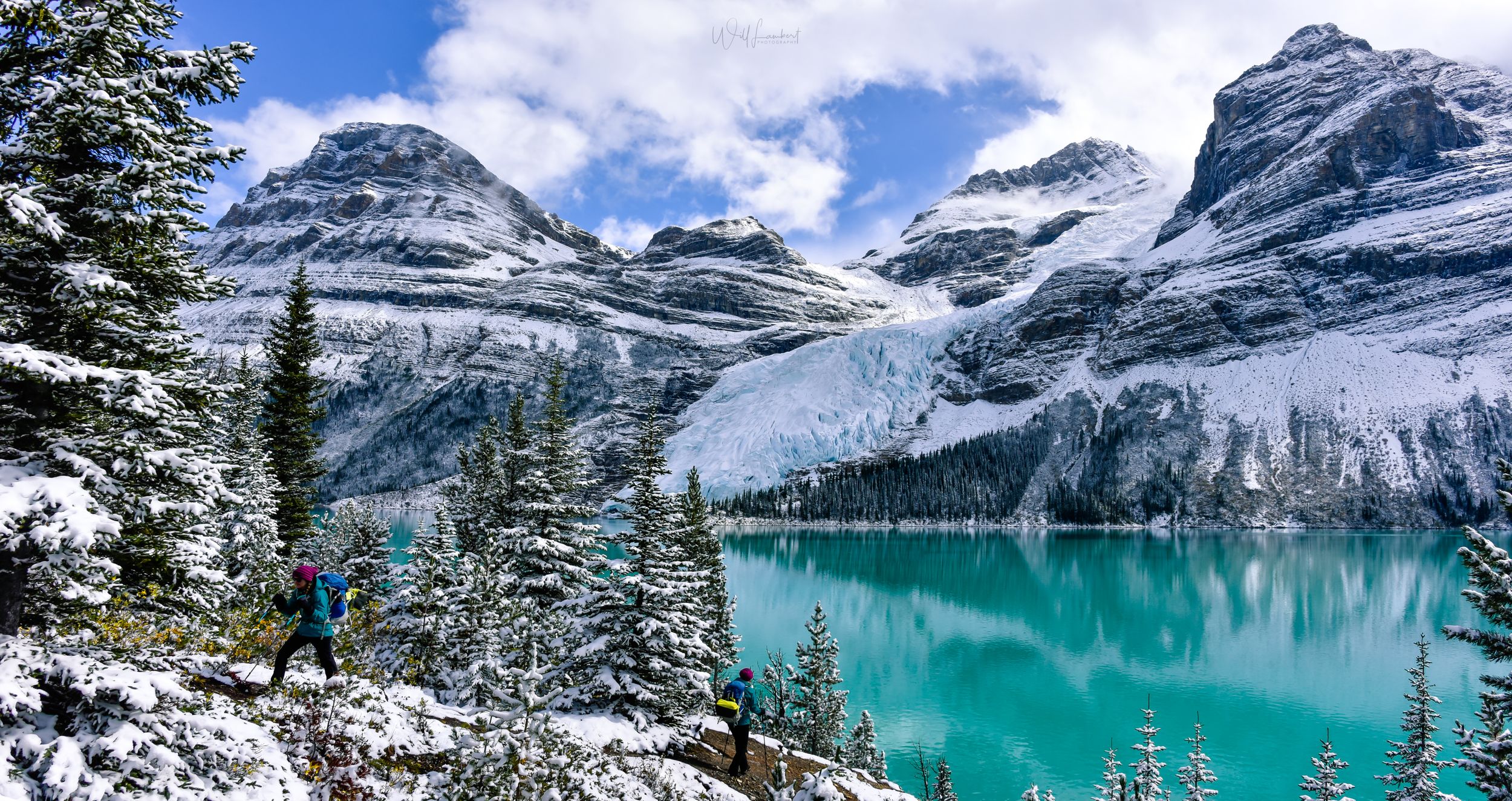 Turquoise alpine lake surrounded by snow-capped mountains and evergreen trees in the Canadian Rockies.