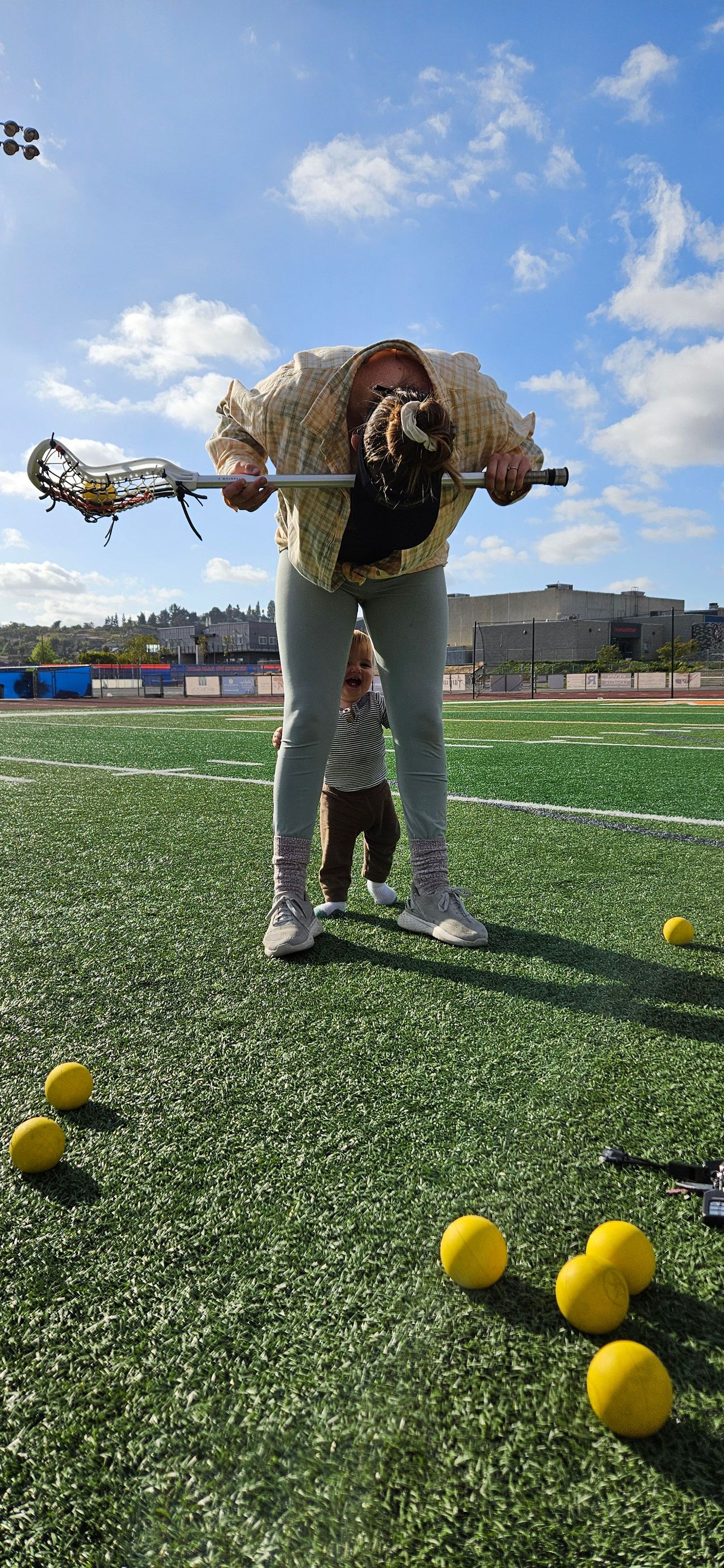 Lacrosse player demonstrates technique with equipment on sports field with yellow balls scattered.