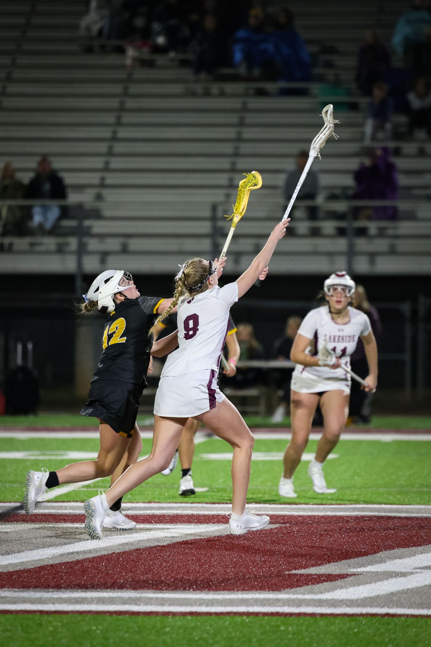 Lacrosse players jump and compete for ball during intense game action.