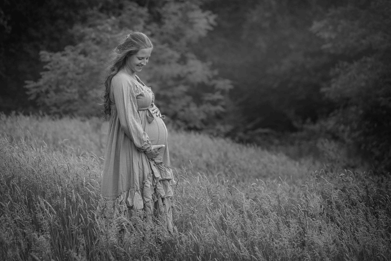 Zwart-wit foto van een zwangere vrouw in een lang kleed, staand in een veld.