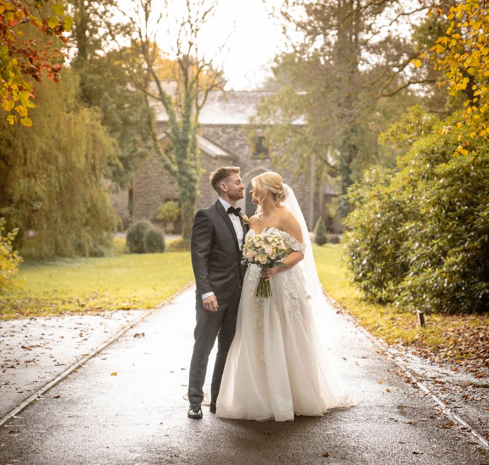 Wedding portraits on a path with beautiful fall foliage and stone buildings in the background.