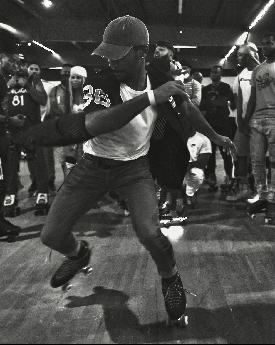 Roller skater in baseball cap and athletic wear performs dance moves on wooden floor.