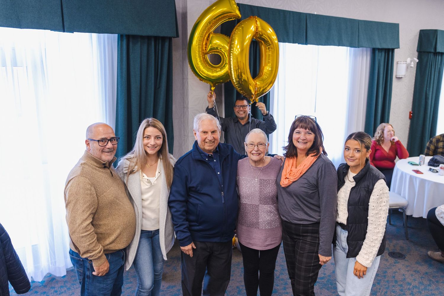 A group poses together at a celebration with a large gold number 60 balloon decoration in the background.