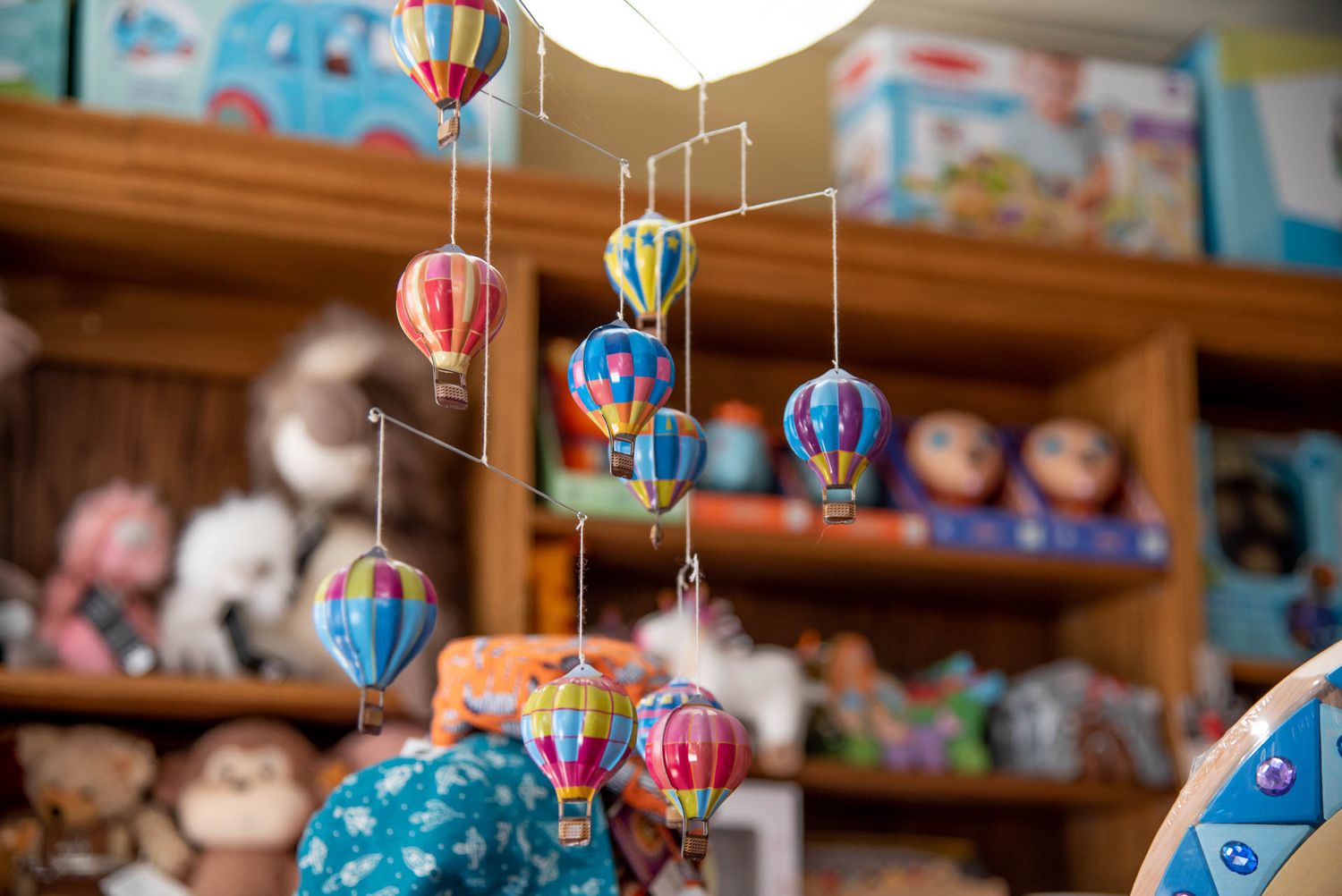 Colorful hanging mobile of miniature hot air balloons displayed in a toy store with wooden shelves in the background.