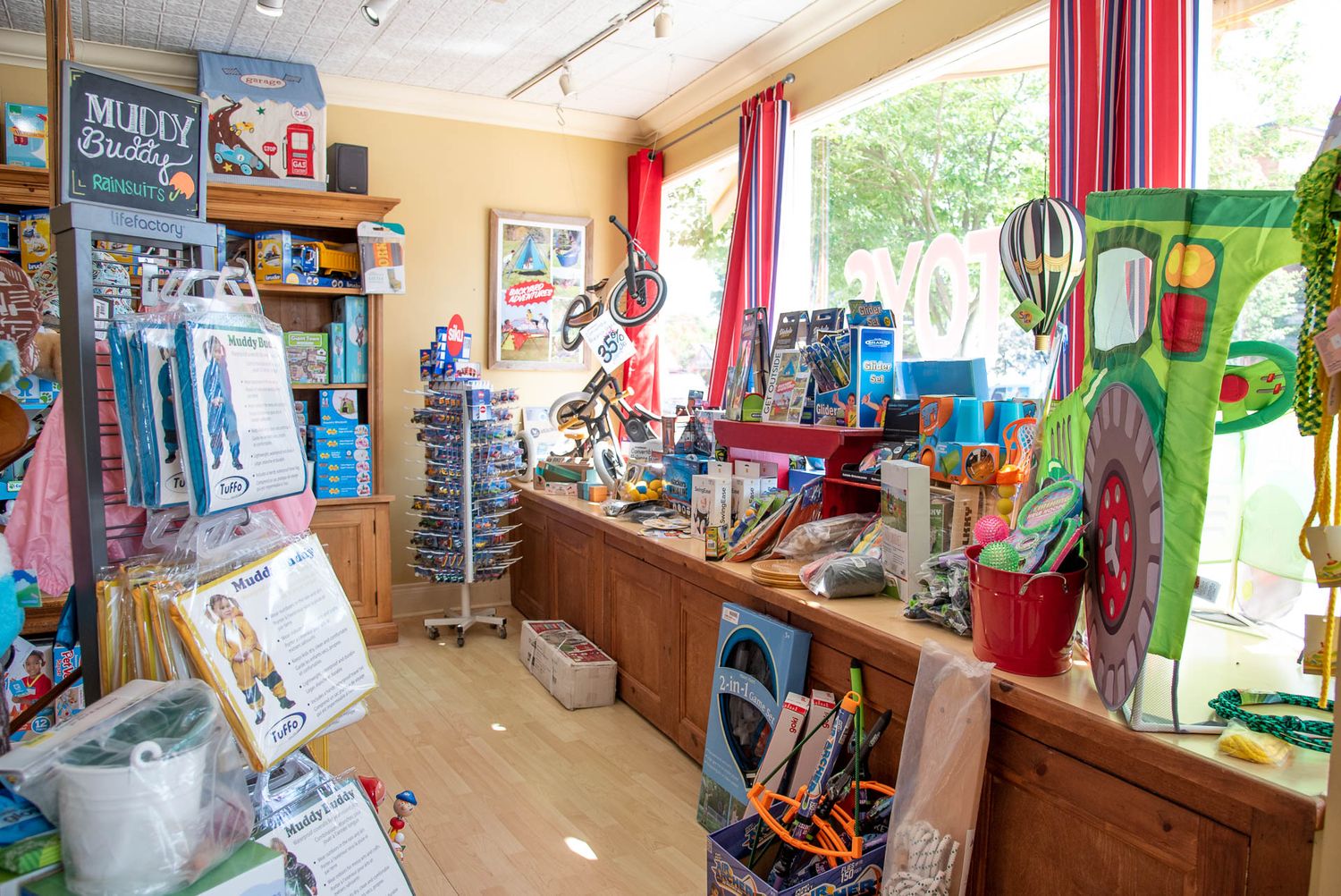 Cozy retail shop interior with colorful curtains, shelves stocked with merchandise, and natural light from windows.