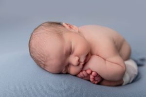 A sleeping newborn baby with delicate features rests peacefully on soft blue fabric.