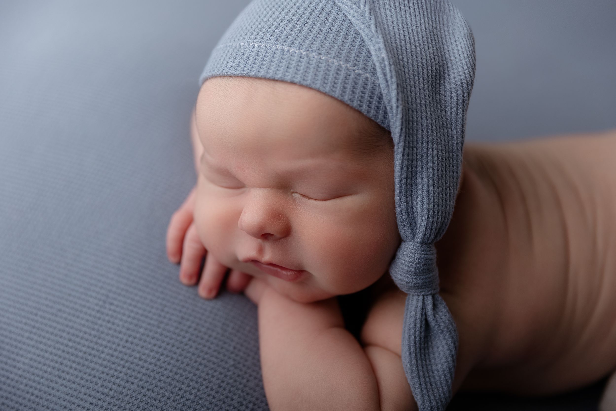 Sleeping newborn baby wearing soft gray knit hat resting on textured gray fabric in a peaceful pose.