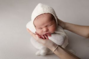 Curled up newborn infant sleeping on soft blue surface wearing white diaper.