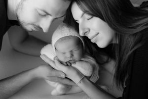 Intimate black and white portrait of new parents tenderly cradling their sleeping newborn.
