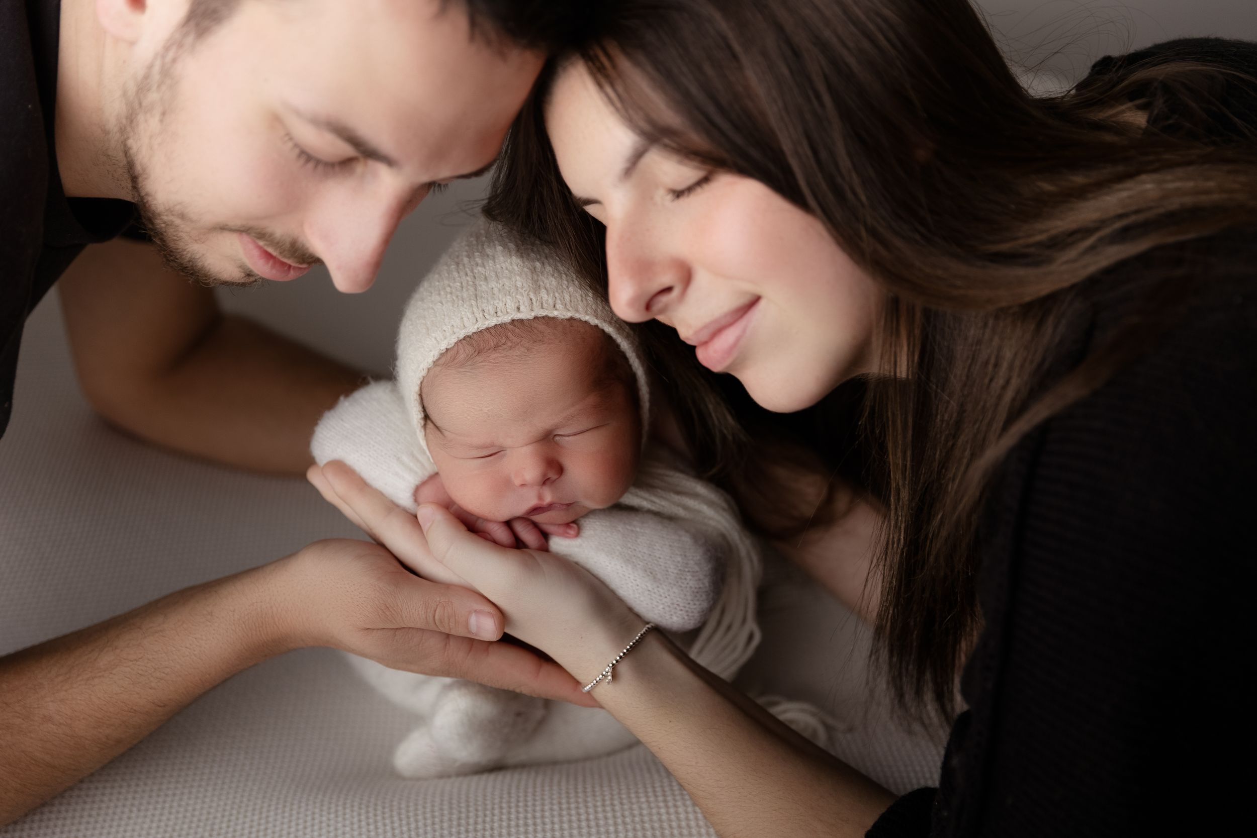Parents share an intimate moment with their sleeping newborn baby dressed in soft white knitwear.