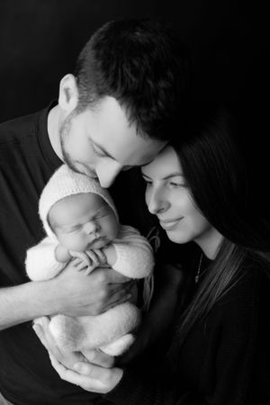 Black and white portrait of a couple lovingly admiring their newborn baby swaddled in white.