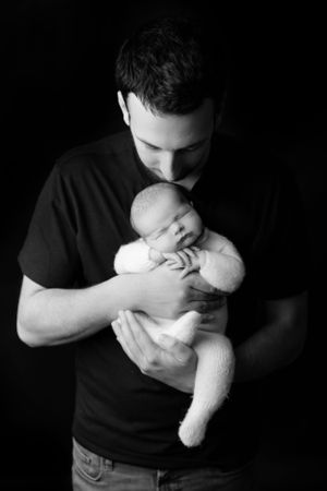 Black and white portrait of loving parent in dark shirt tenderly holding and gazing down at sleeping newborn baby.