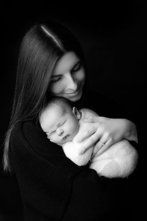 Black and white portrait of a tender moment between adult and sleeping newborn captured in soft studio lighting.