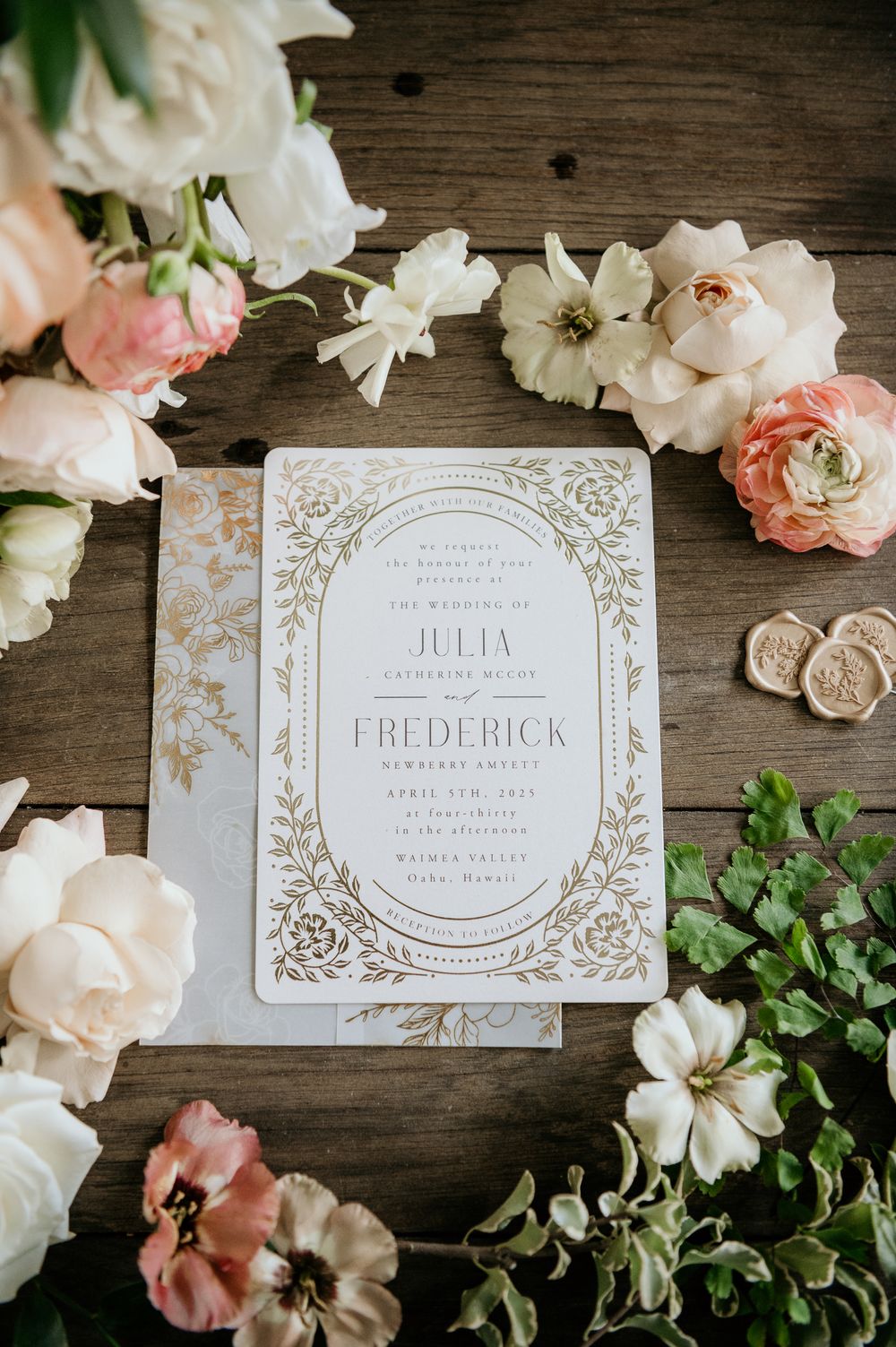 Elegant wedding invitation with gold floral design surrounded by blush pink and white flowers on wooden surface.