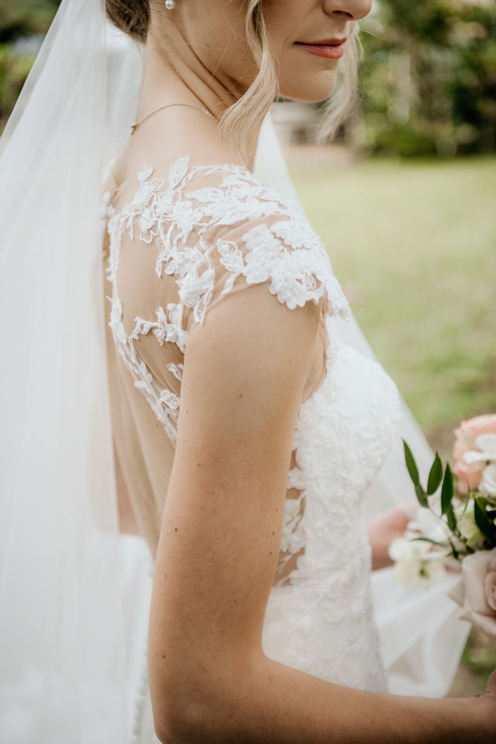Close-up detail of delicate white lace on a wedding dress with sheer illusion neckline and flowing veil.