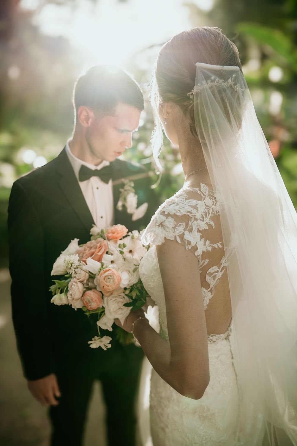 A romantic wedding moment captured at sunset with a bride in lace holding a peach and white bouquet.