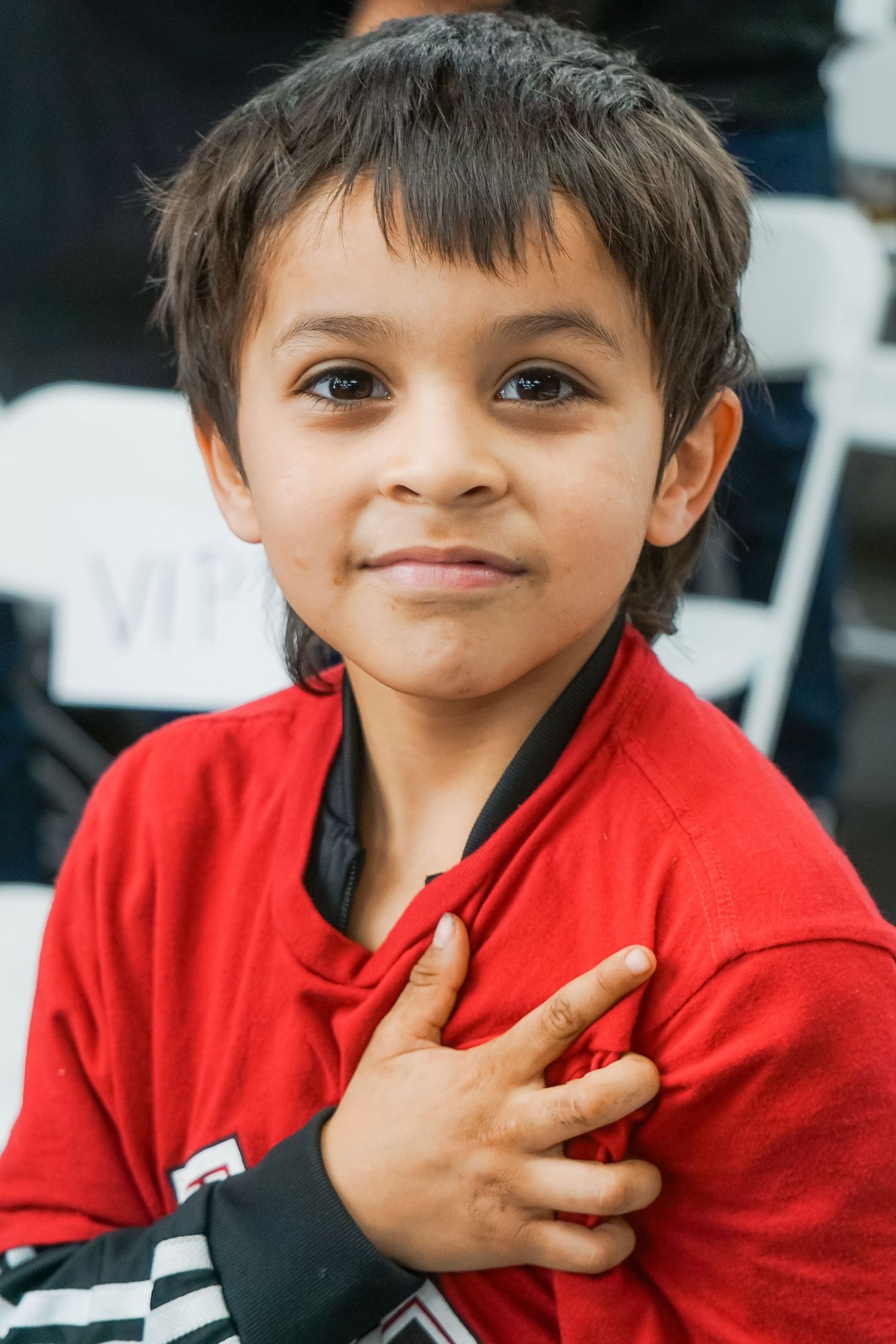 Young child in a bright red jacket smiles at the camera while placing hand over heart.