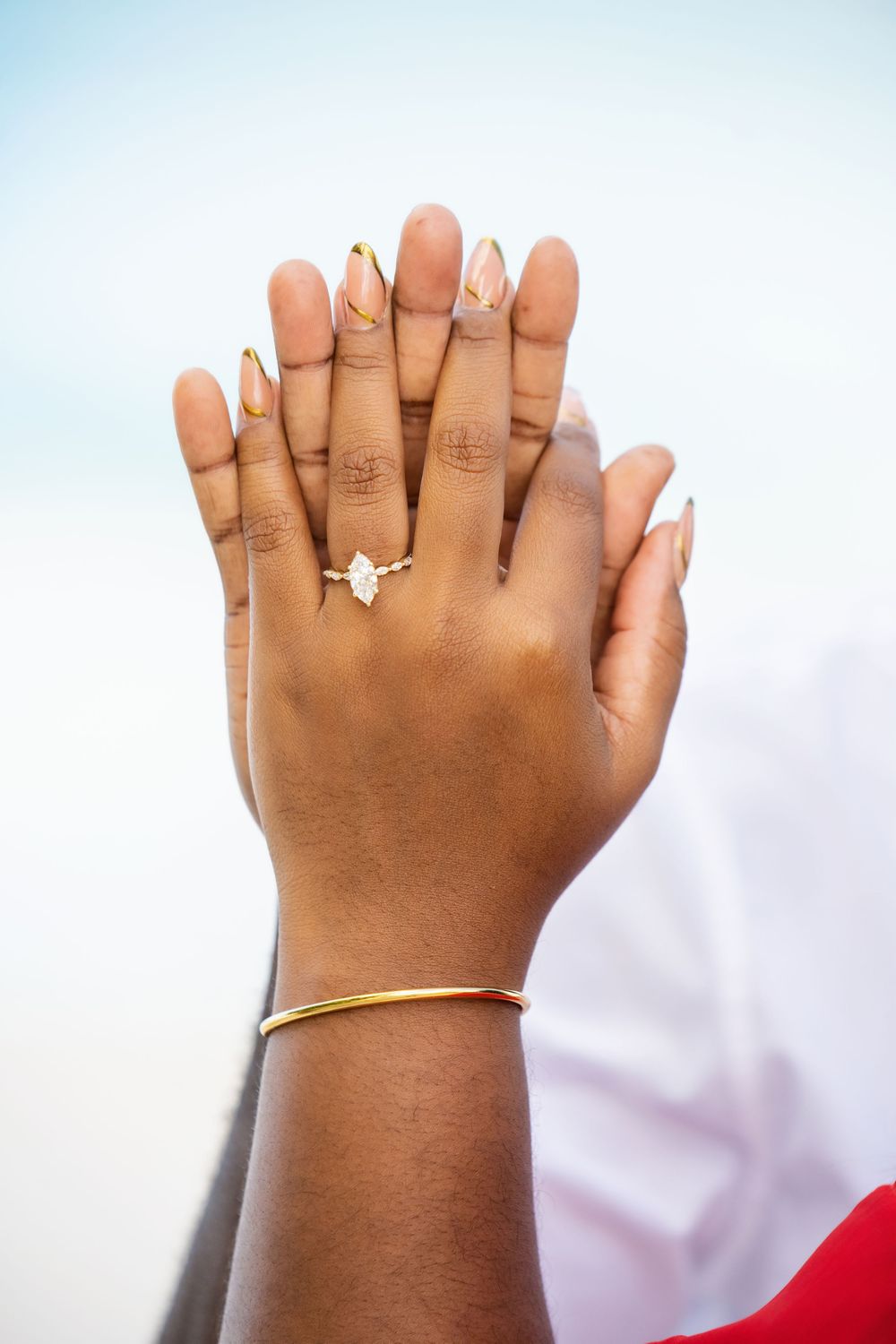 Close up of hands with French manicure and butterfly ring against light background.