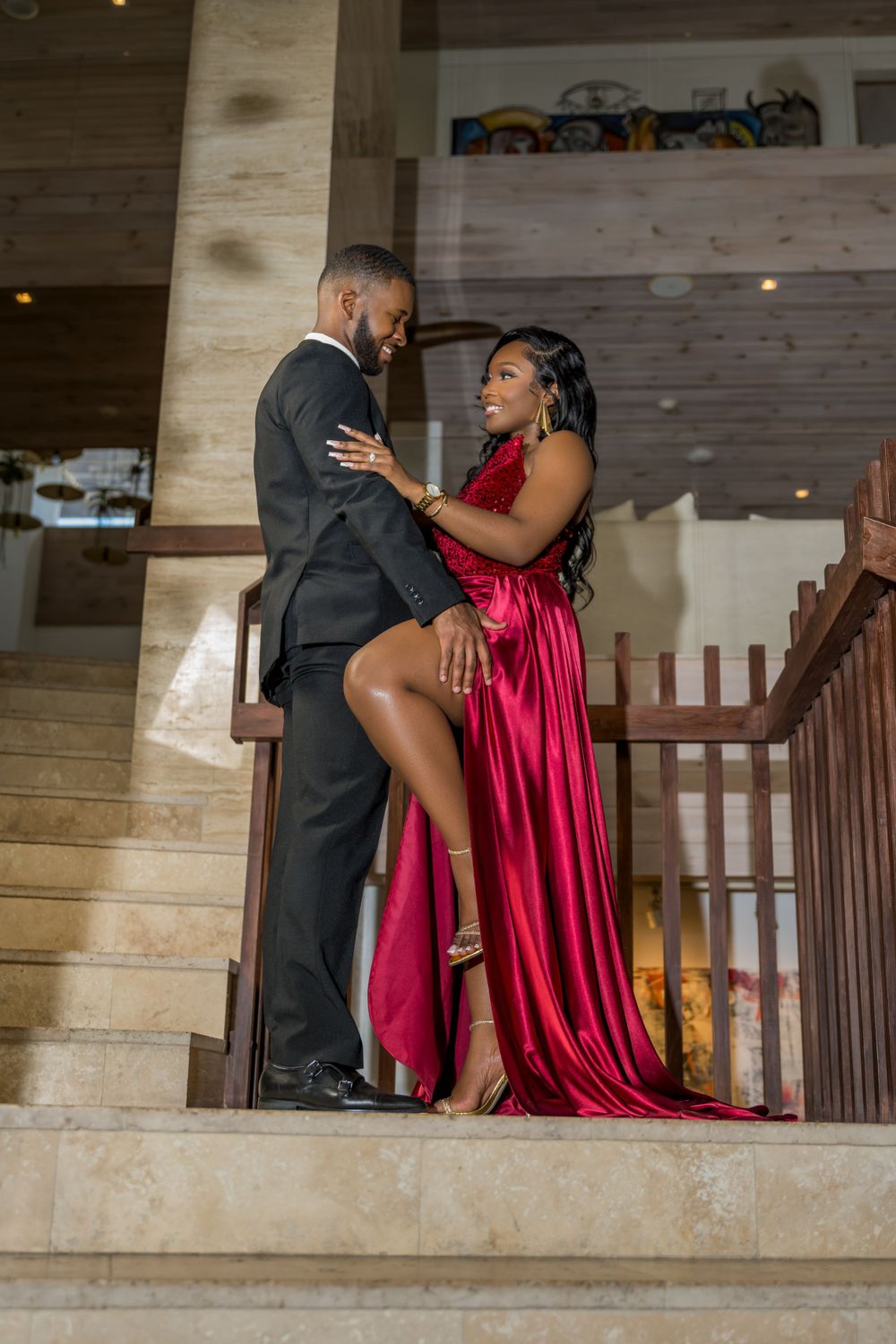 Romantic couple pose on stairs with woman in flowing red evening gown.