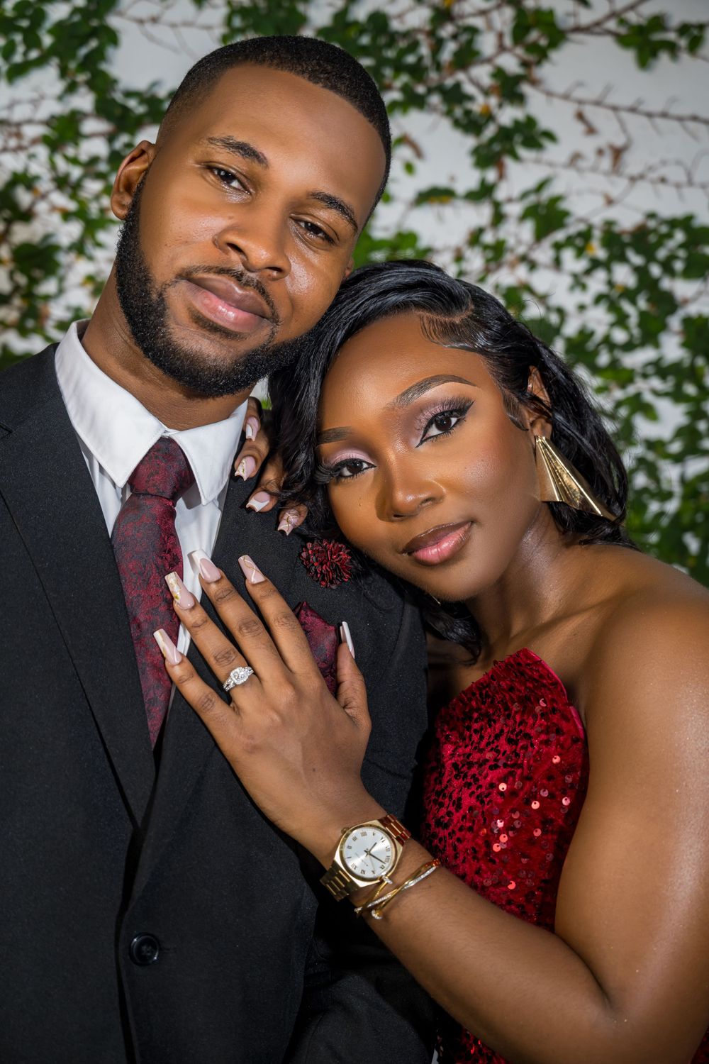 Formal couple portrait showing engagement ring against floral backdrop.