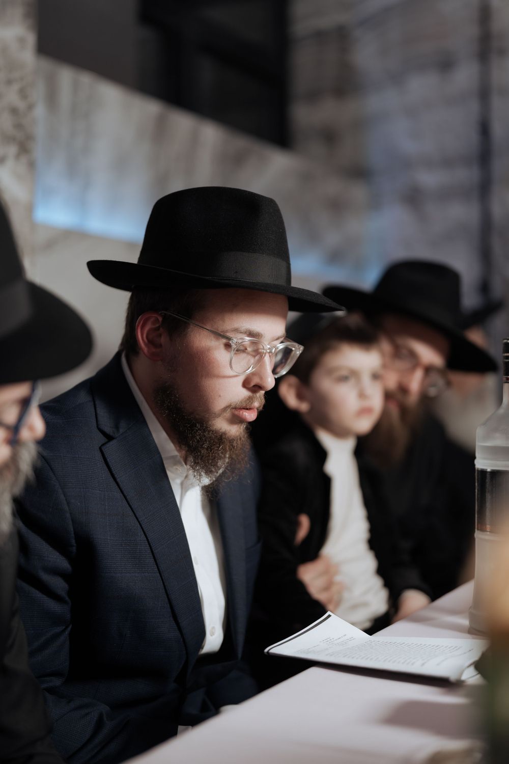 Orthodox Jewish men in black hats study religious texts together at a table.
