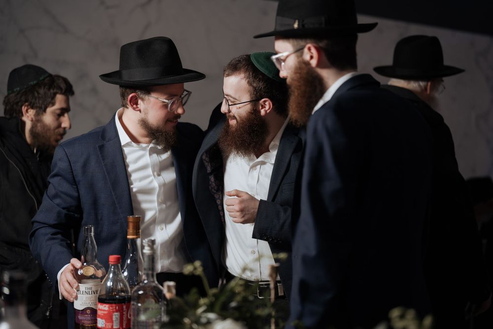 Men in traditional Orthodox attire gather around a table having an animated discussion.