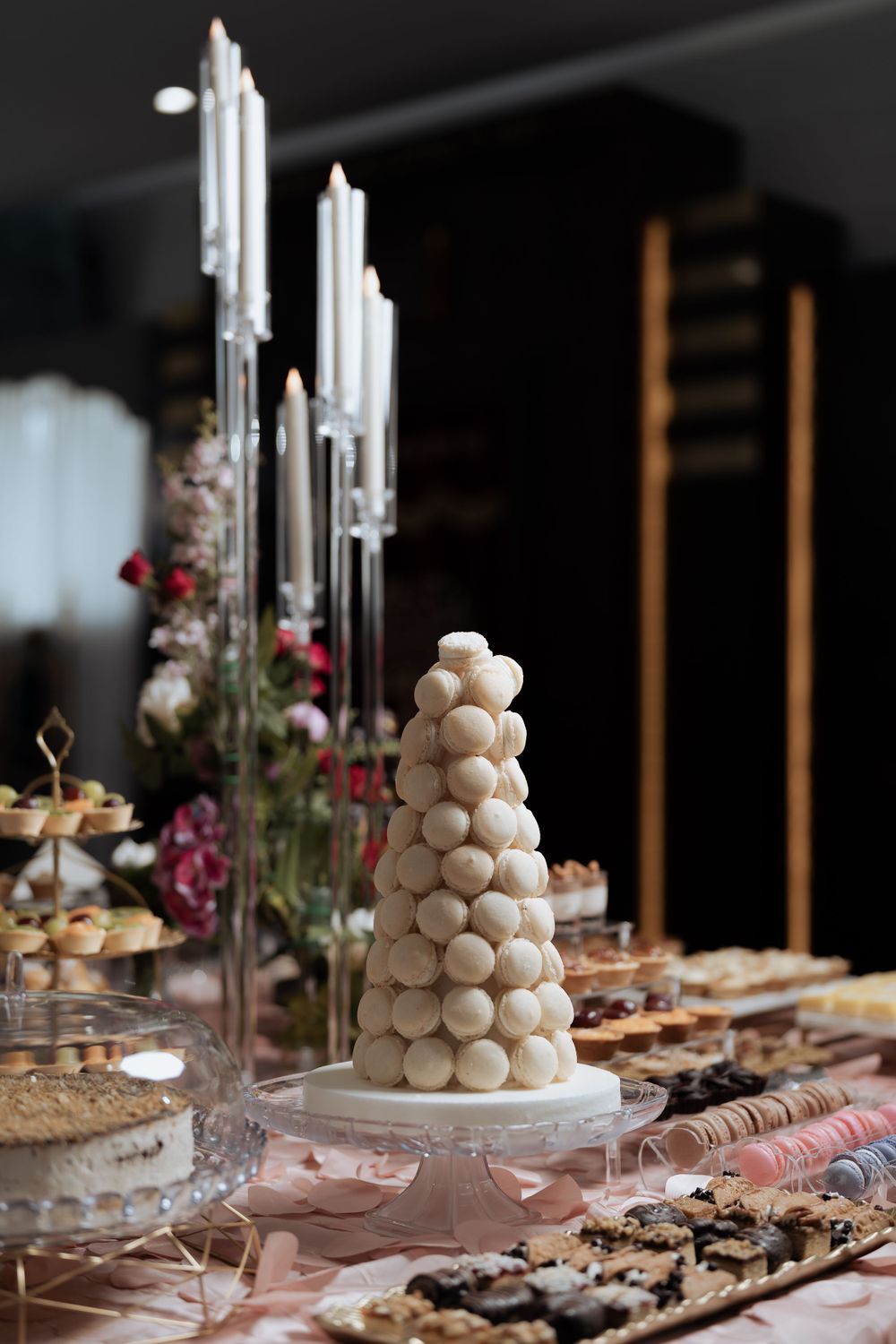 Modern wedding dessert table with tall silver candles and a white macaron tower centerpiece.