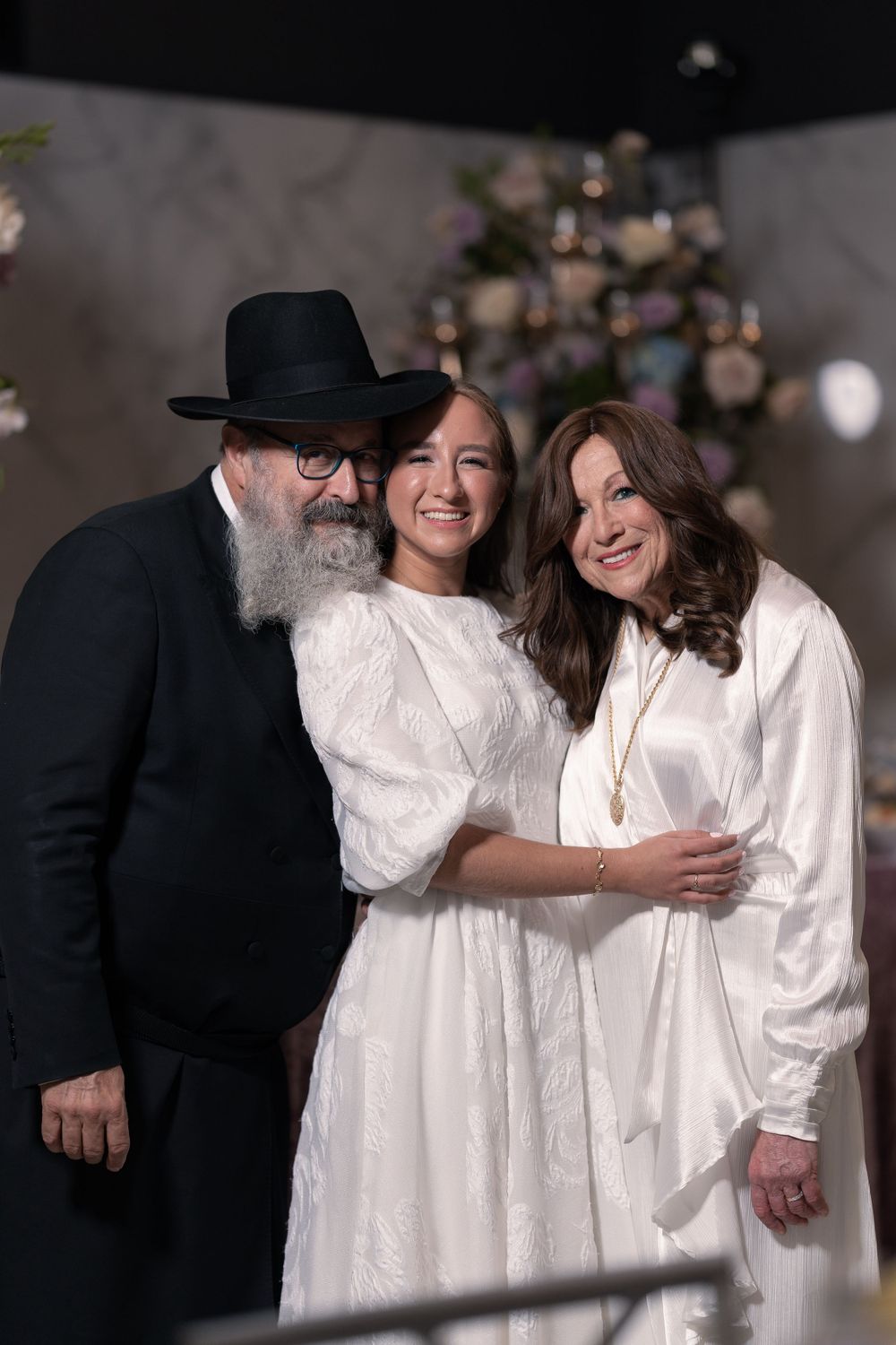 Three people pose together at a formal event against a floral backdrop.