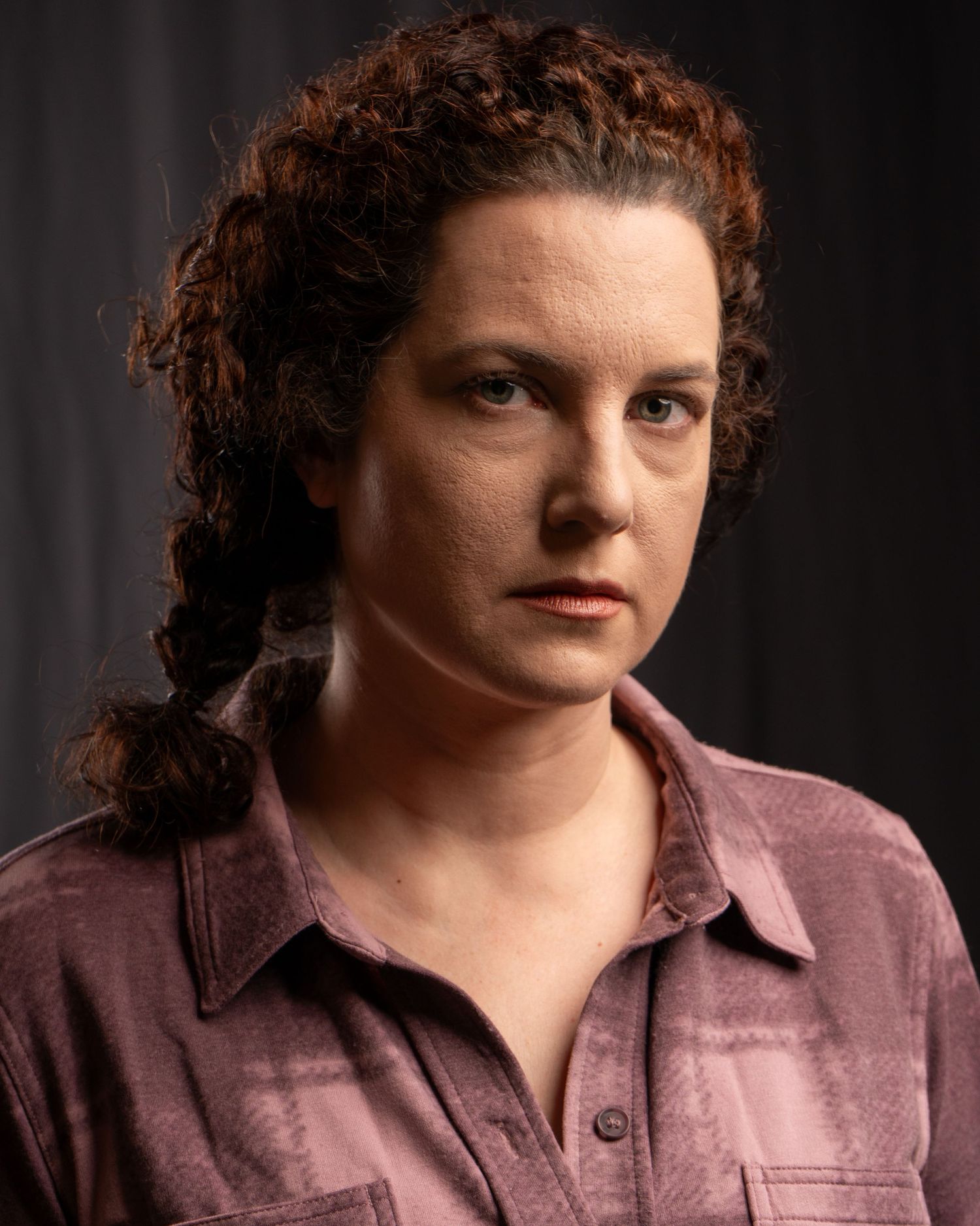 Portrait of person in pink button-down shirt with curly hair against dark background.