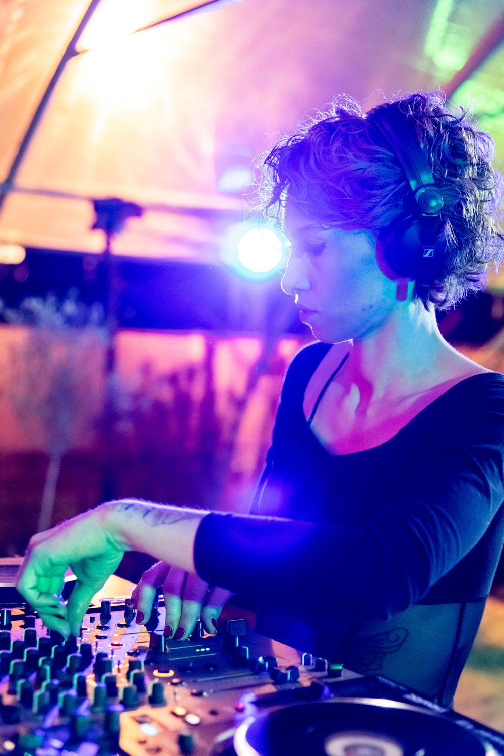 DJ performing at a nightclub with vibrant purple and green lighting while mixing on professional equipment.