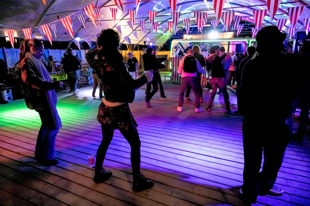 People dancing on a wooden deck under colorful neon lights at a nighttime outdoor party.