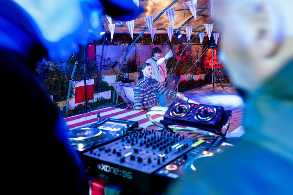 DJ performs at a nightclub with professional equipment bathed in blue and red lighting during a live set.