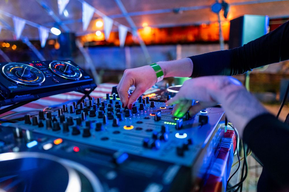 DJ hands adjusting controls on professional mixing board with blue lighting at nightclub event.