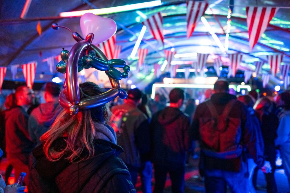 A crowd celebrates at a nightclub decorated with American flags while bathed in red and blue lights and neon glow.