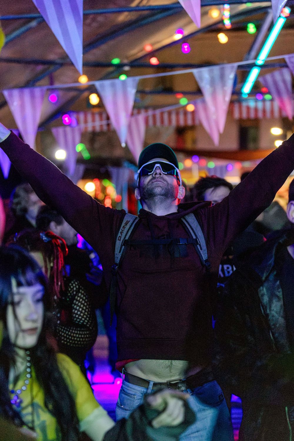 A person dances with arms raised at a nightclub under colorful lights and hanging decorations.
