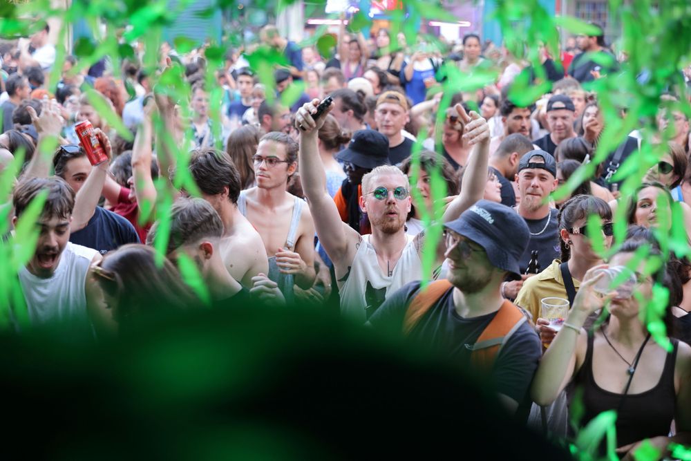 Excited crowd celebrating at an outdoor event with green confetti falling in the foreground.