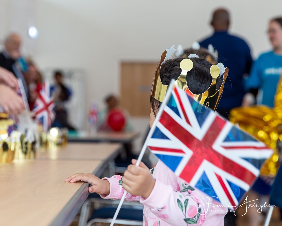 Person waving a Union Jack flag and wearing a gold crown at a community celebration event.