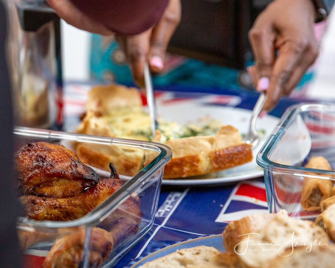Party guests reach for food served in glass dishes at a casual dining table with colourful placemats.