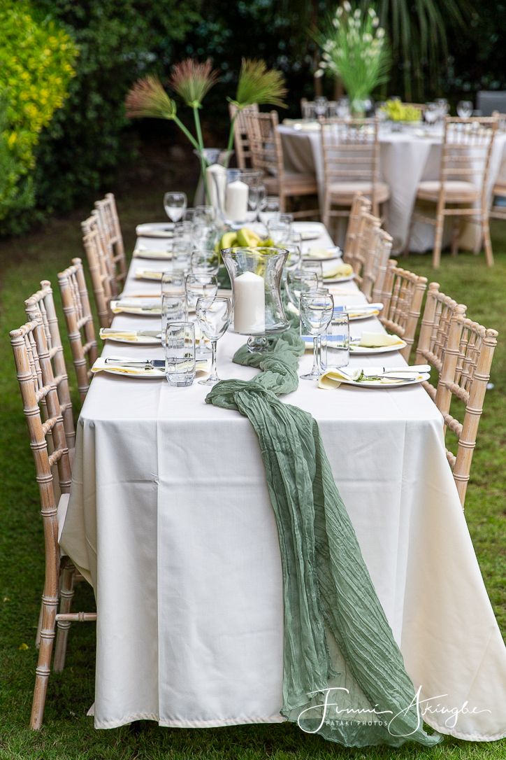 Elegant garden party table setting with white linens, rustic chairs, and sage green runner.