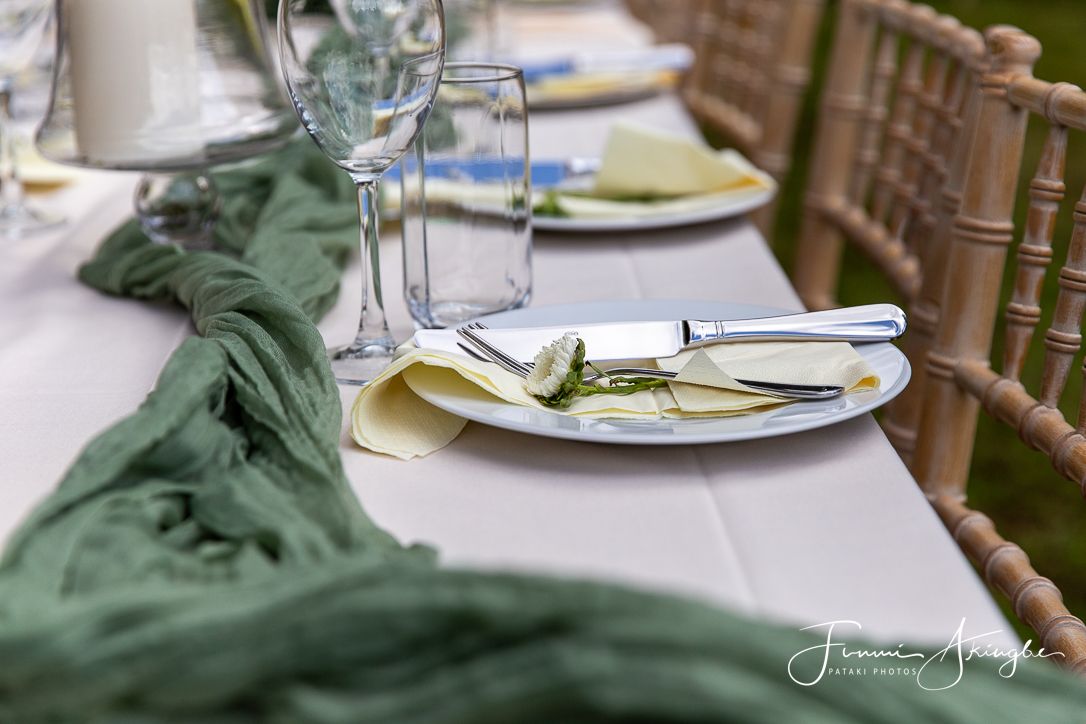 Elegant garden party table setting with flowing sage green fabric runner, gold chairs and white place settings.