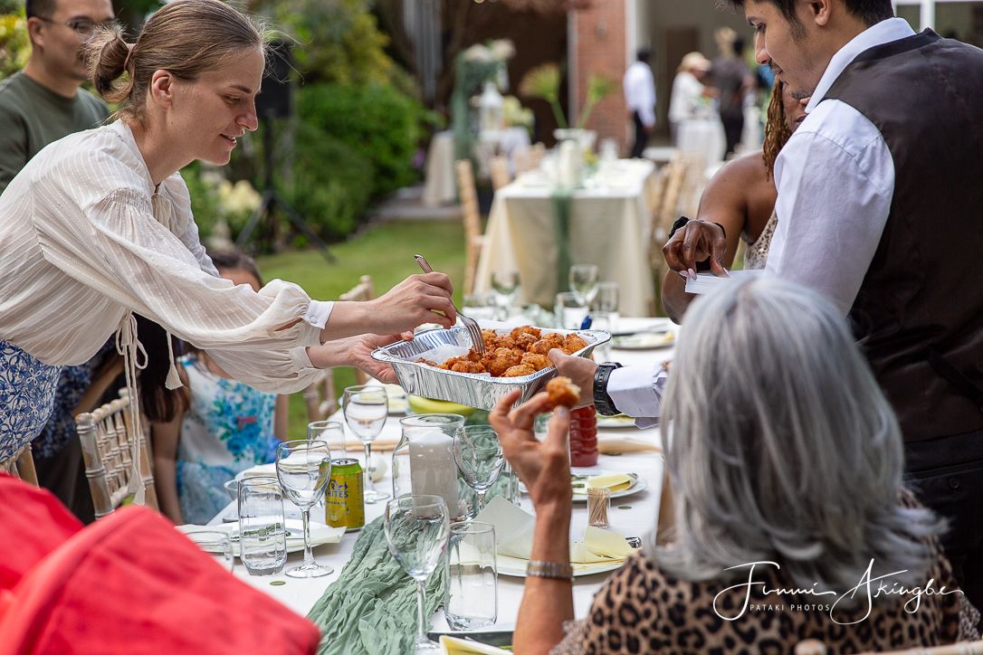 A group of people enjoying a  garden party with table service and food being served in a garden setting.